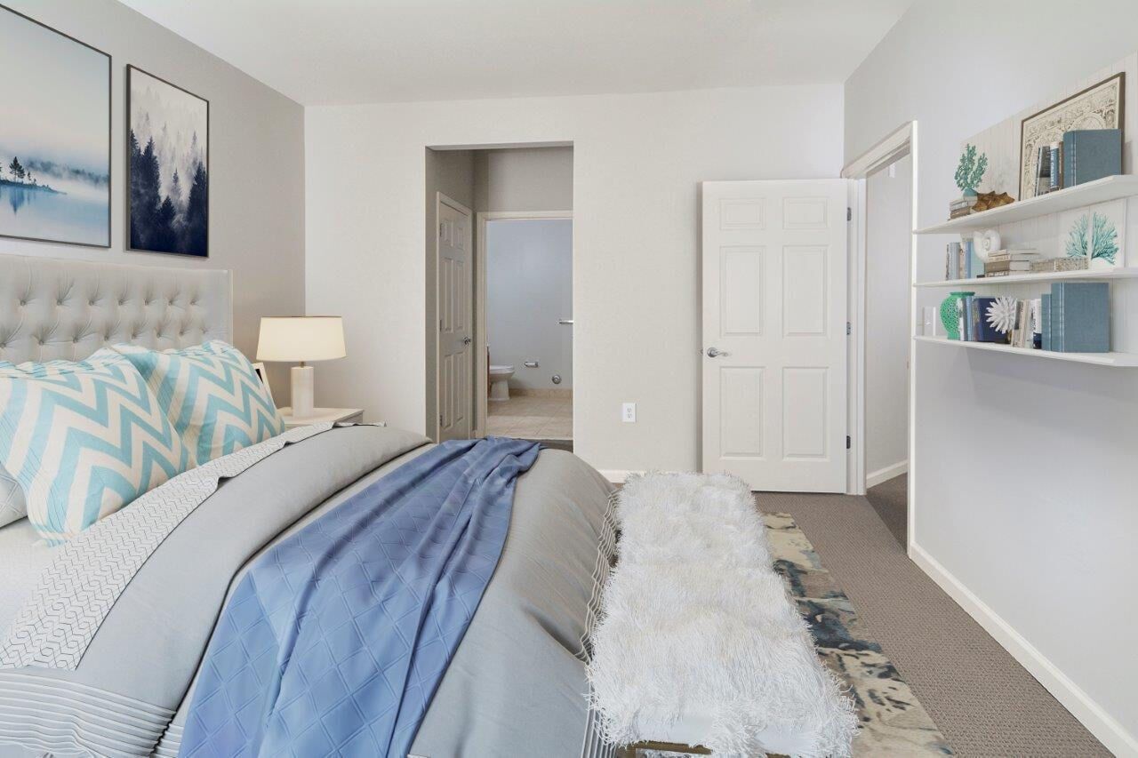 Bedroom in a modern apartment with a tufted headboard, blue bedding, and a white bookshelf.
