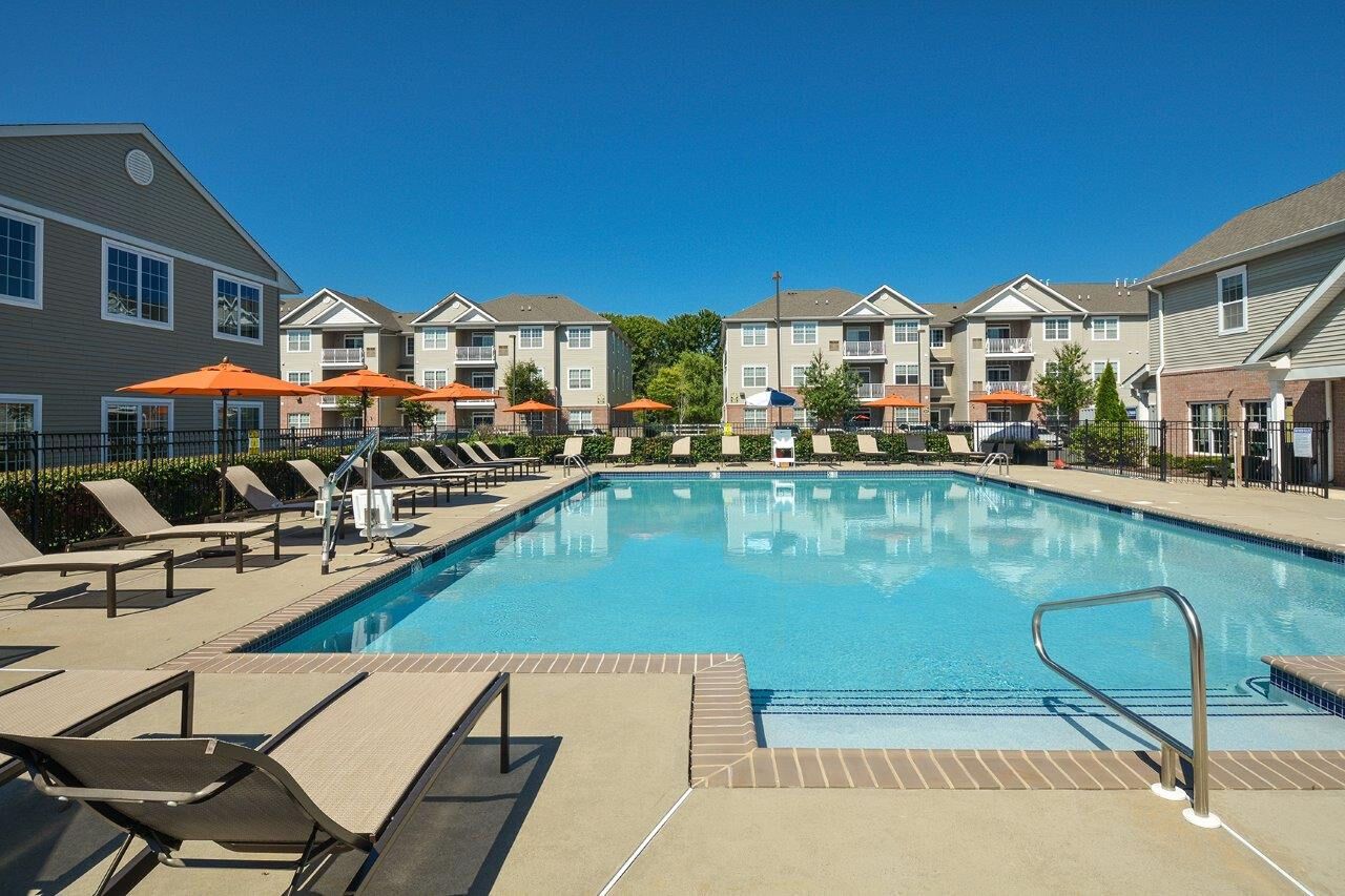 Outdoor community pool with lounge chairs and orange umbrellas, surrounded by apartment buildings.