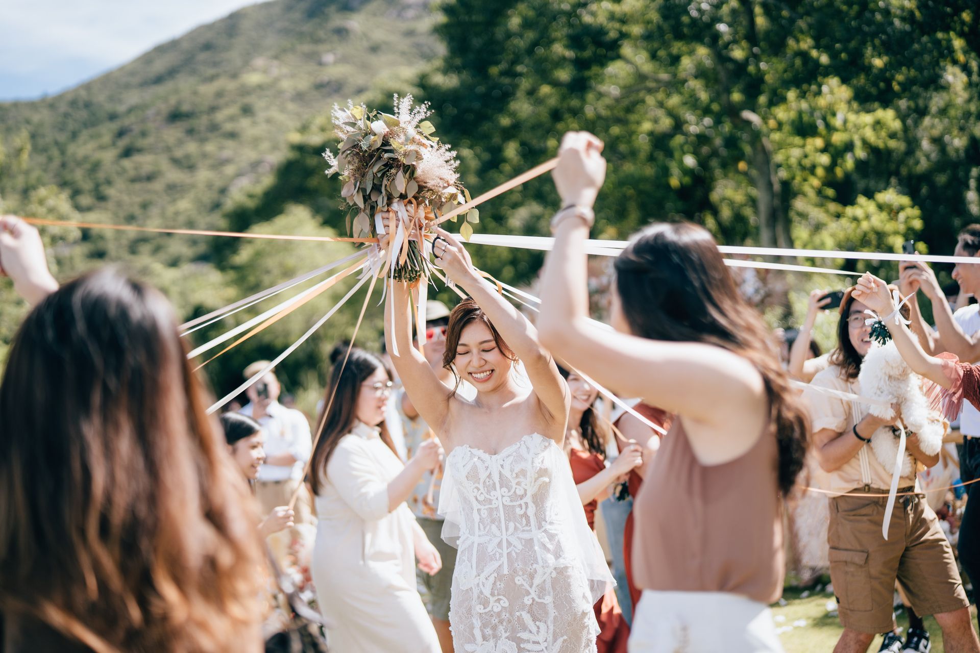 Bride raises bouquet while guests dance with ribbons at an outdoor wedding.