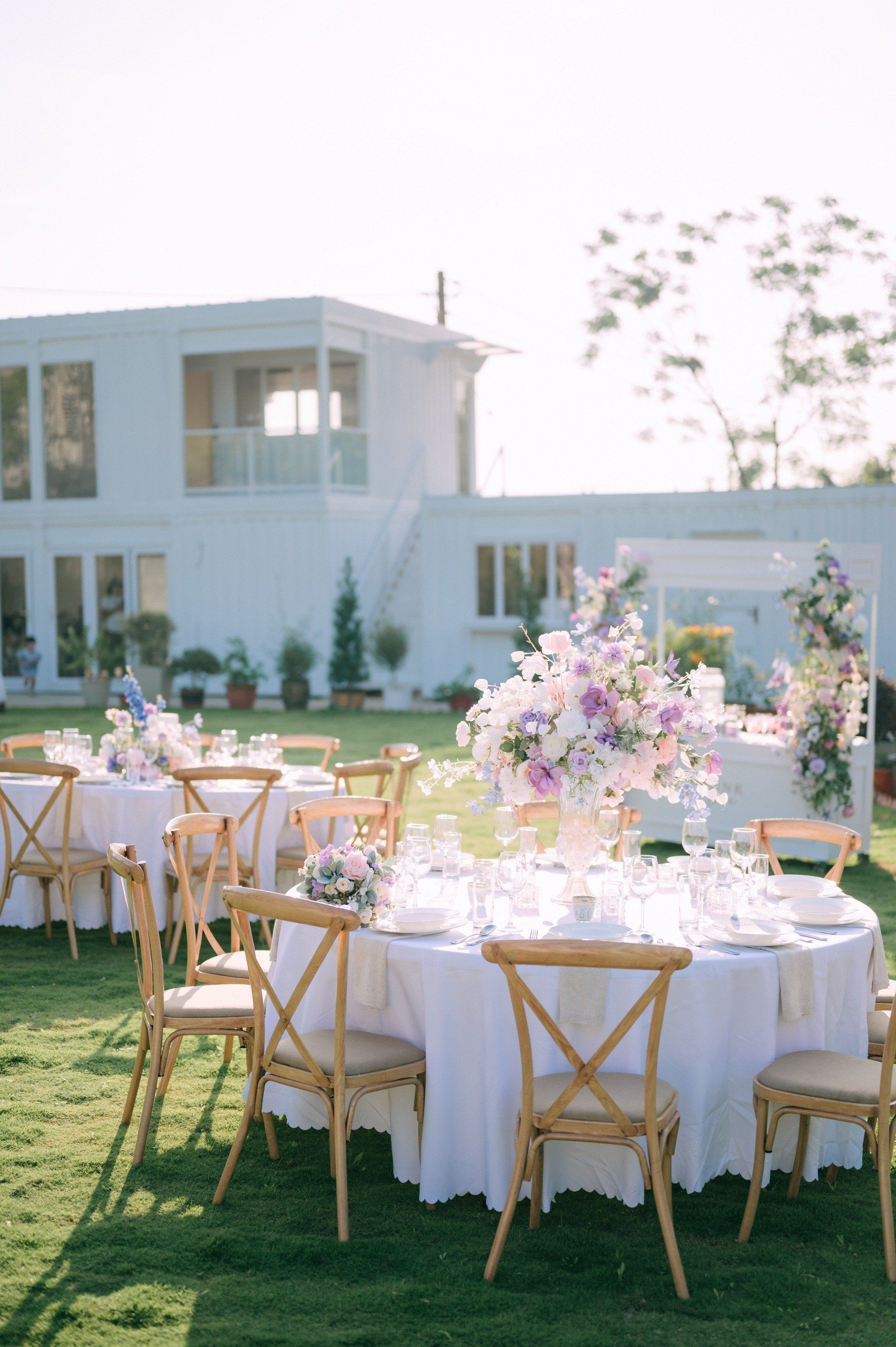 Outdoor wedding reception with round tables set with white linens and flower centerpieces.