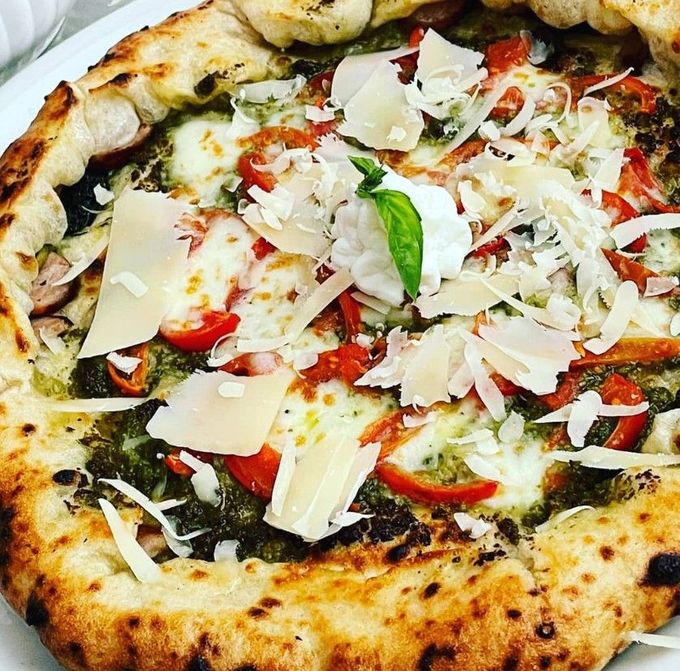 Primo piano di una pizza margherita condita con basilico, mozzarella, salsa di pomodoro e scaglie di parmigiano.