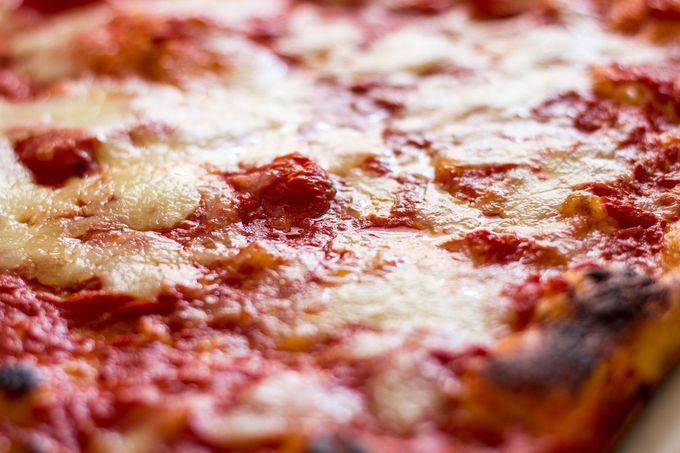 Primo piano di una pizza Margherita con salsa di pomodoro, mozzarella fusa e foglie di basilico su una crosta bruciacchiata.