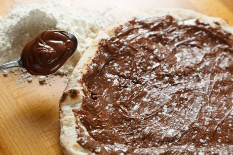 Un cucchiaio di crema al cioccolato spalmabile accanto a una fetta di pane ricoperta di cioccolato