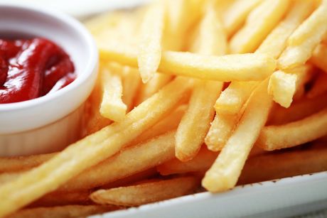 Patatine fritte accanto a una tazza di ketchup su un piatto bianco.