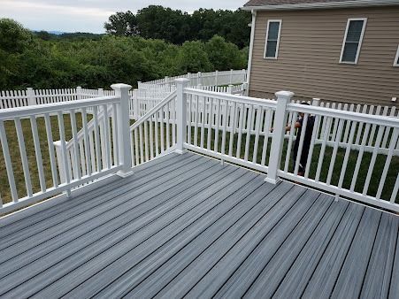 A gray deck with a white railing and a house in the background.
