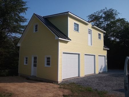 A yellow house with three garage doors and a black roof