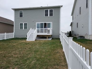 The backyard of a house with a white picket fence and a deck.