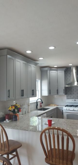 A kitchen with white cabinets , granite counter tops , a stove , sink , and chairs.