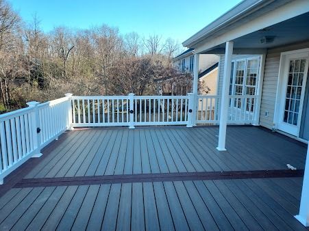 A large deck with a white railing and trees in the background.