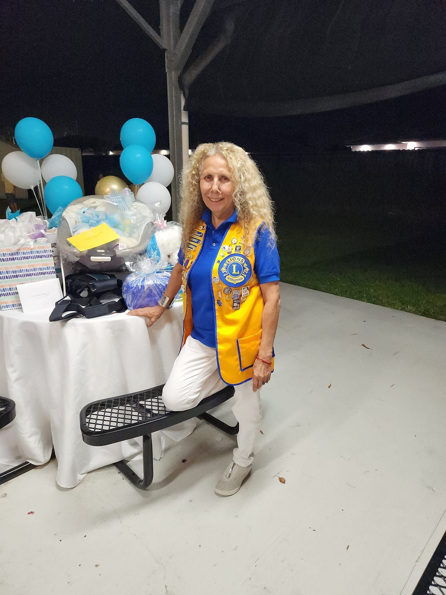 A woman is sitting on a bench in front of a table with balloons.