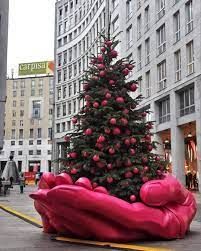 A large pink hand is holding a christmas tree on a city street.