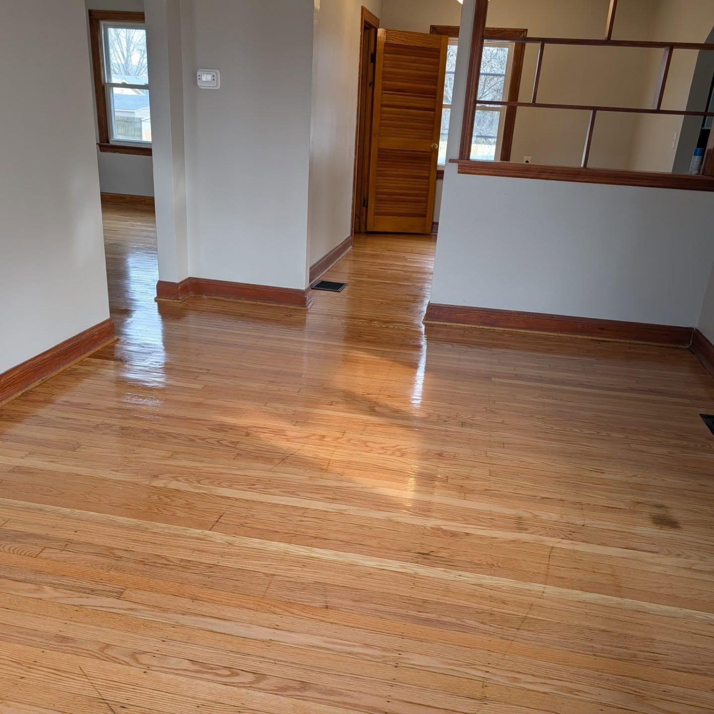 Empty room with polished hardwood floors, gray walls, and a wooden door opening to a hallway