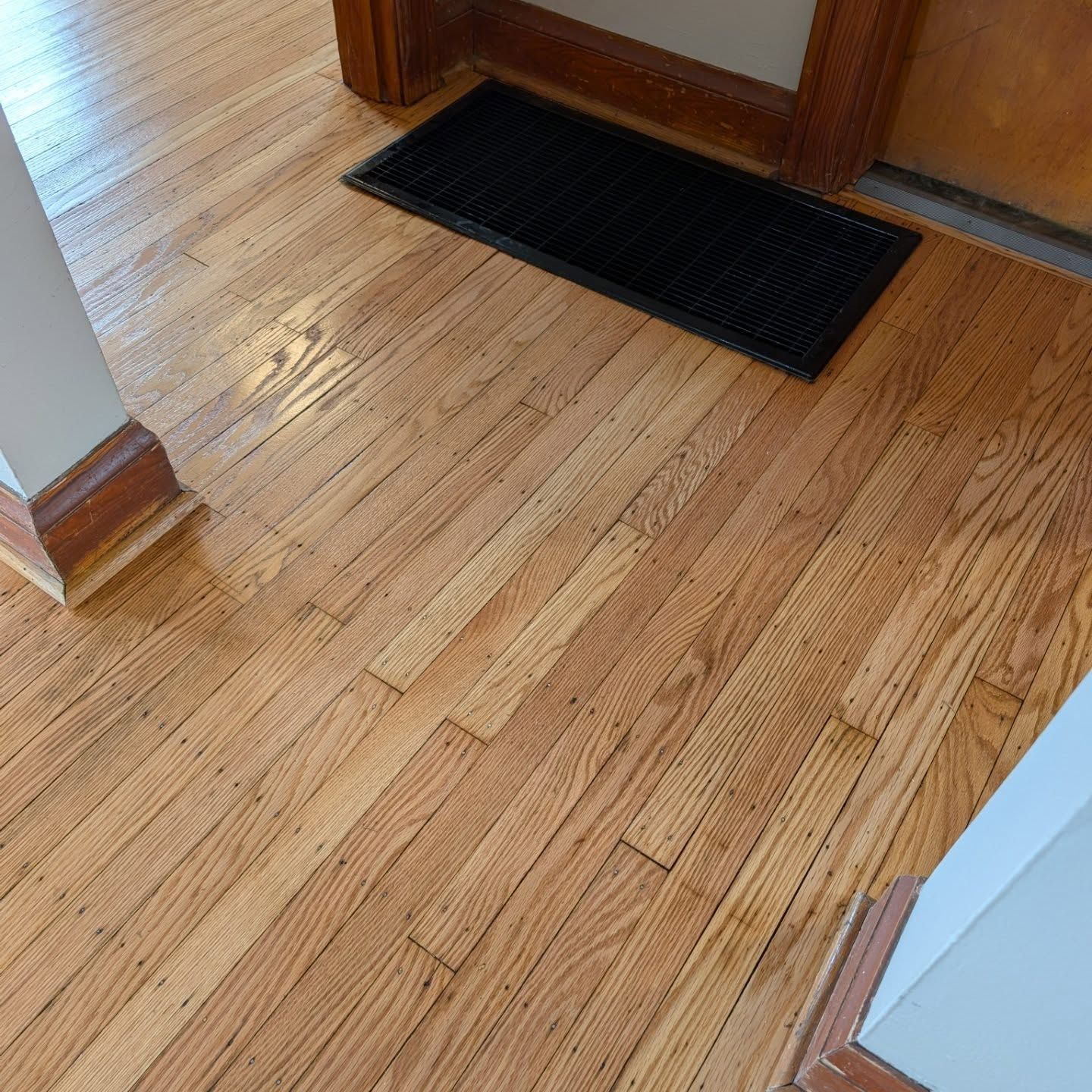 Wooden hallway floor with a black floor mat by a doorway and a stair edge on the left