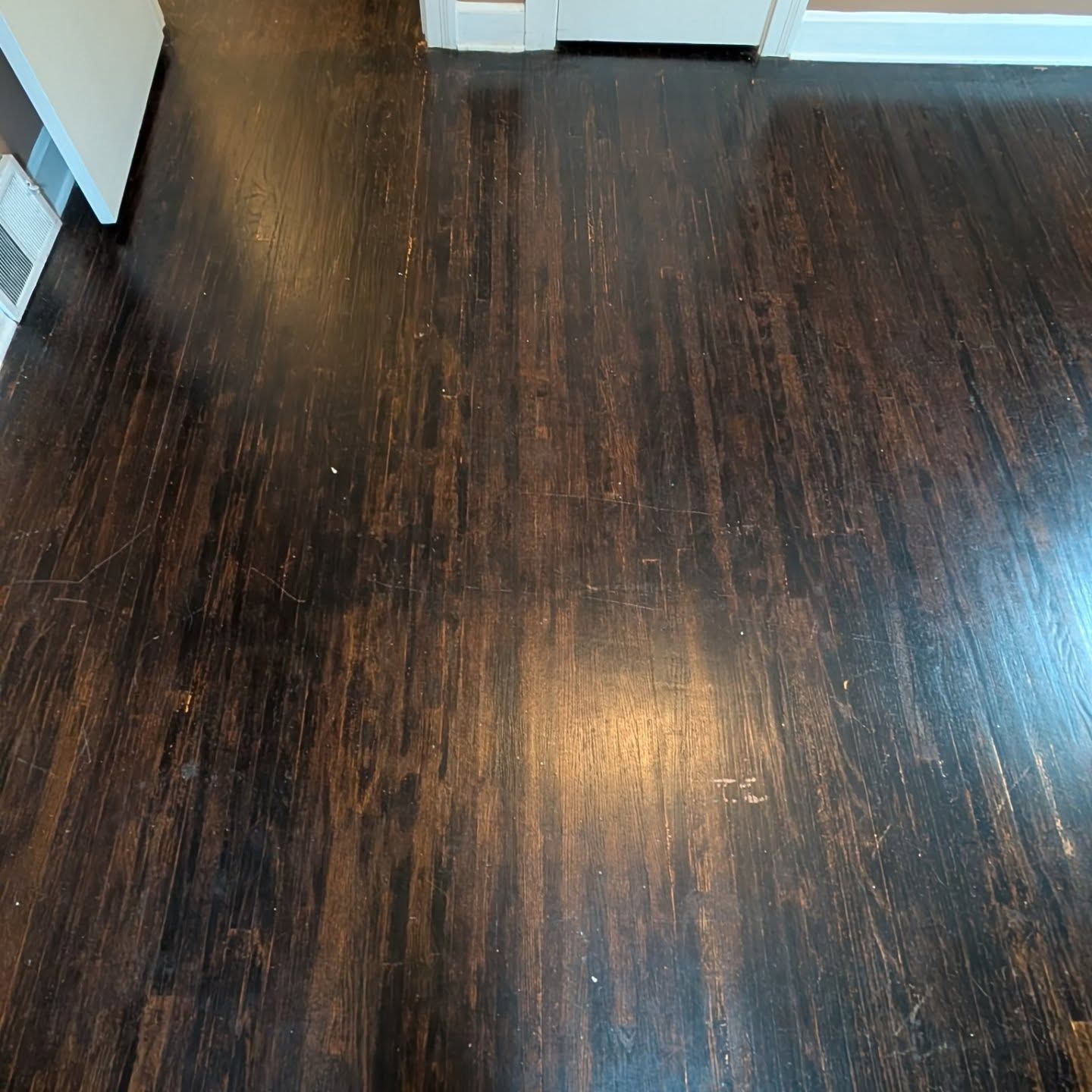 Dark wood floor in a room, with white walls and doorways at the top edge.