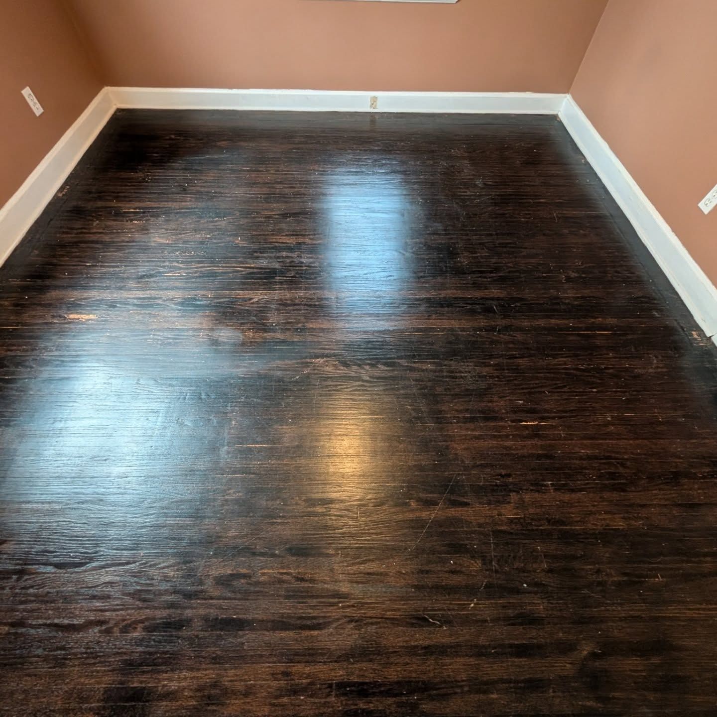 Empty room with dark wood floor, tan walls, and white baseboards.