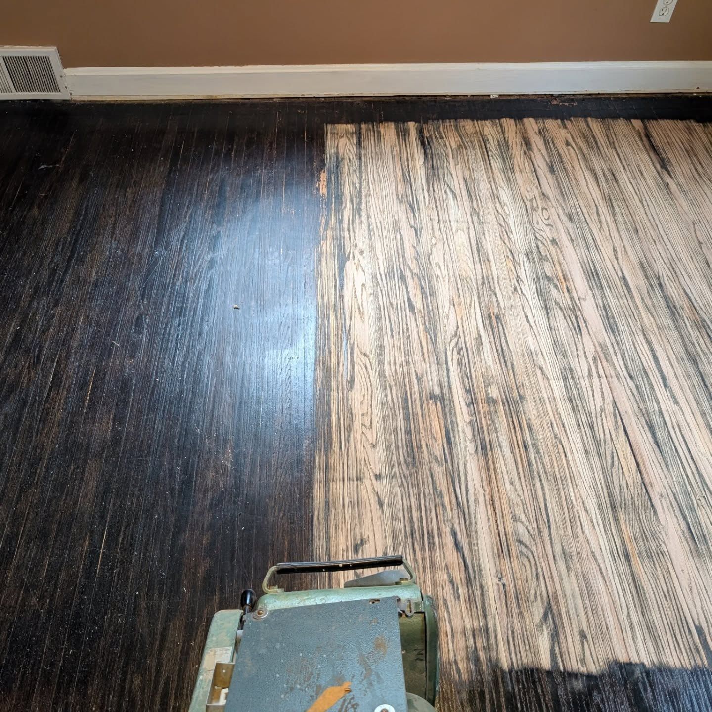 Floor buffer polishing a hardwood floor, half dark and half stripped to bare wood.
