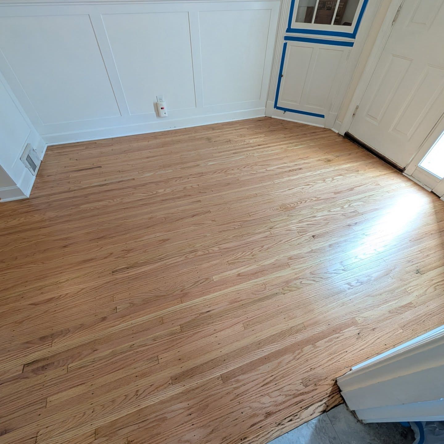 Empty room with light wood floor, white walls, and a sunlit doorway