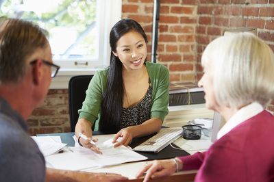 Financial advisor assists elderly couple with documents at a desk in an office.
