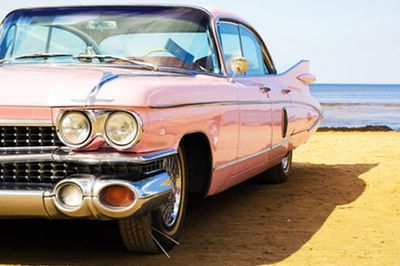 Pink vintage Cadillac parked on a sandy beach with the ocean in the background.
