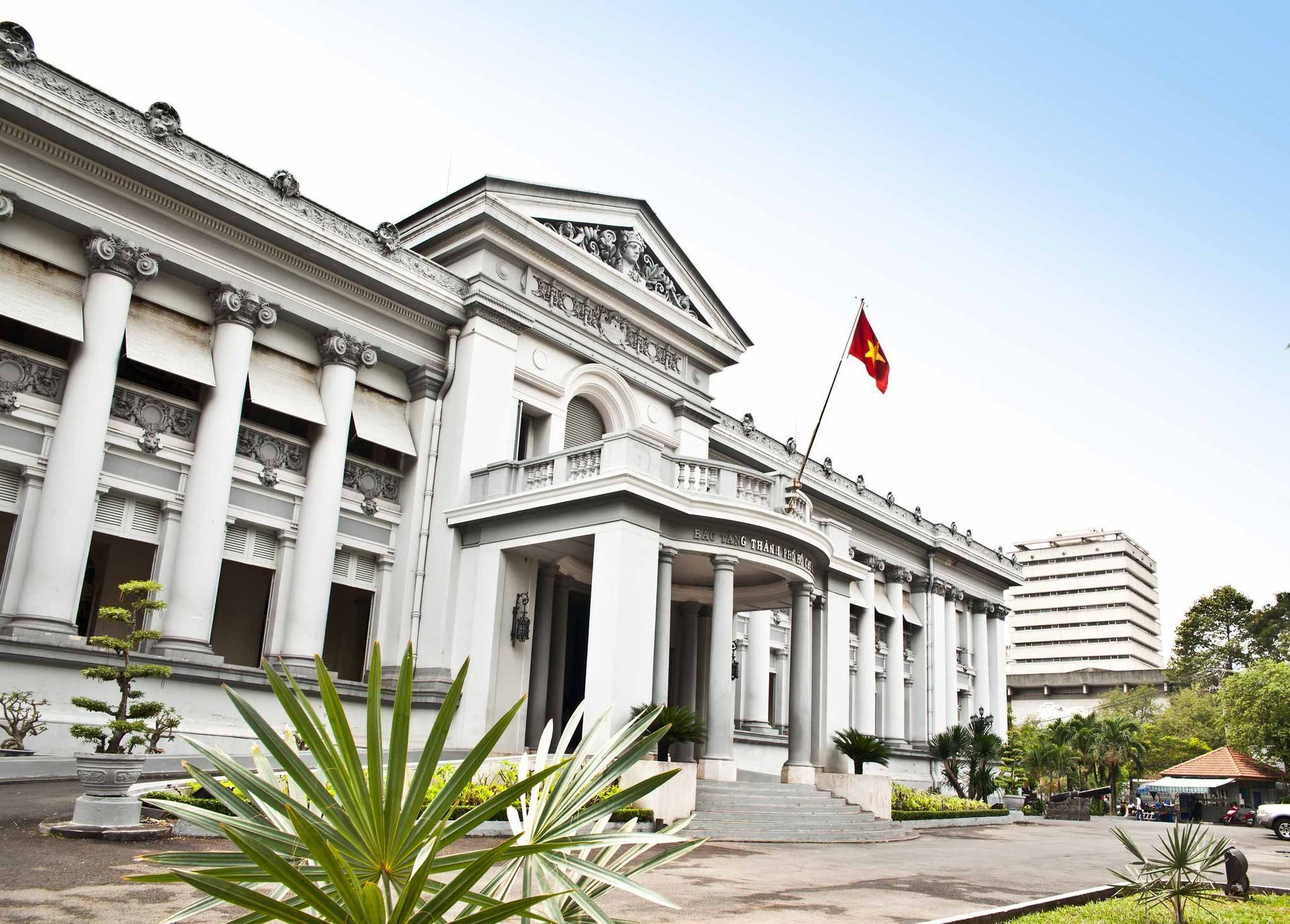 White neoclassical building, Vietnamese flag, lush greenery.