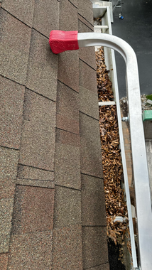 White gutter along the edge of a roof with gray shingles; a curved downspout leads away.