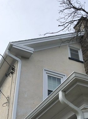 A house with a dark tiled roof and a light-colored exterior against a cloudy sky.