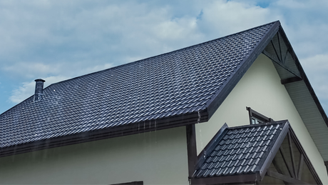 A house with a dark tiled roof and a light-colored exterior against a cloudy sky.