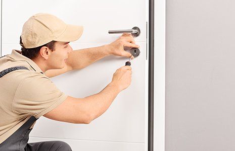 Male locksmith installing a lock on a new door with a screwdriver 