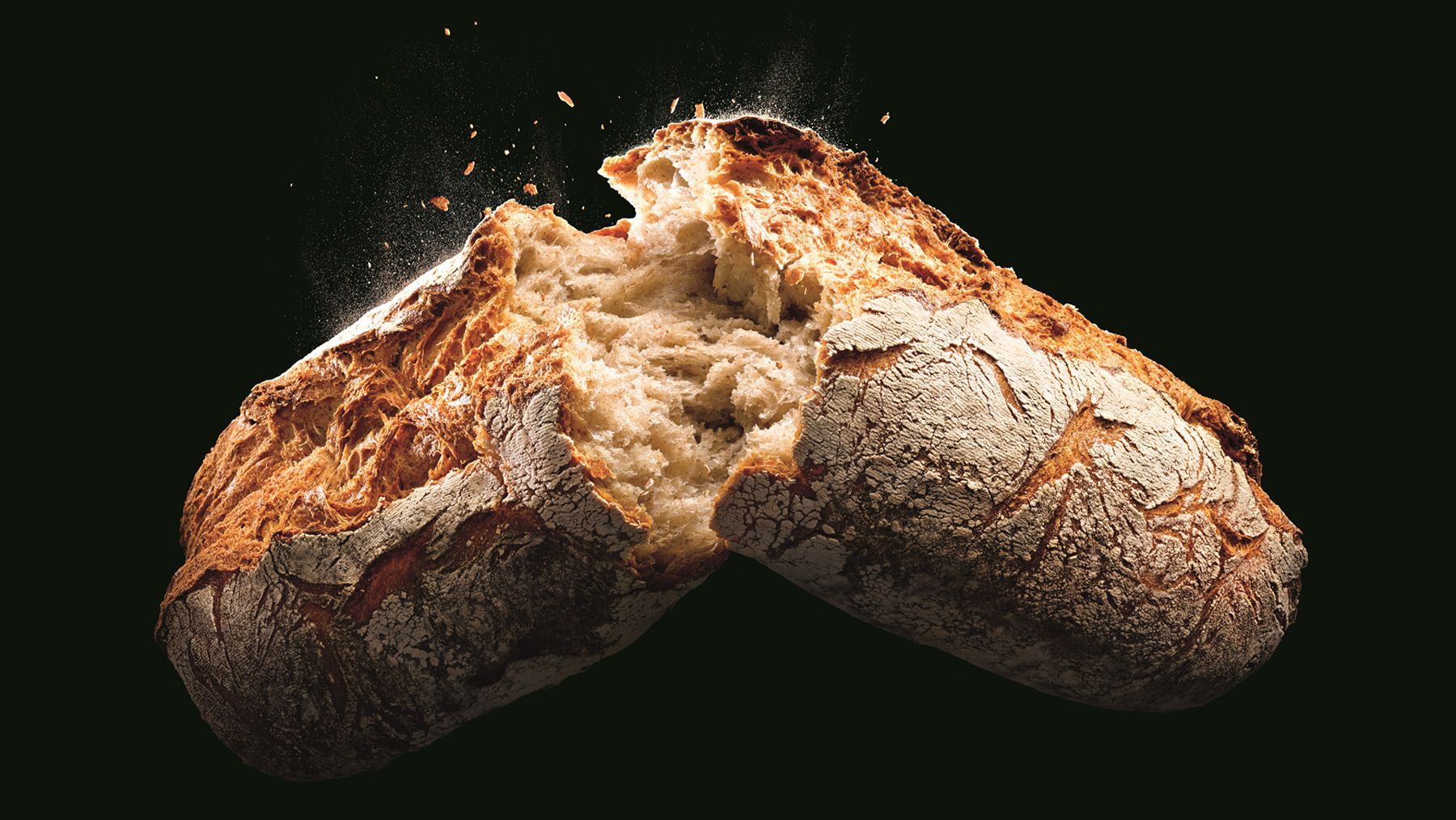 Ein Laib Brot wird auf schwarzem Hintergrund in zwei Hälften geschnitten.