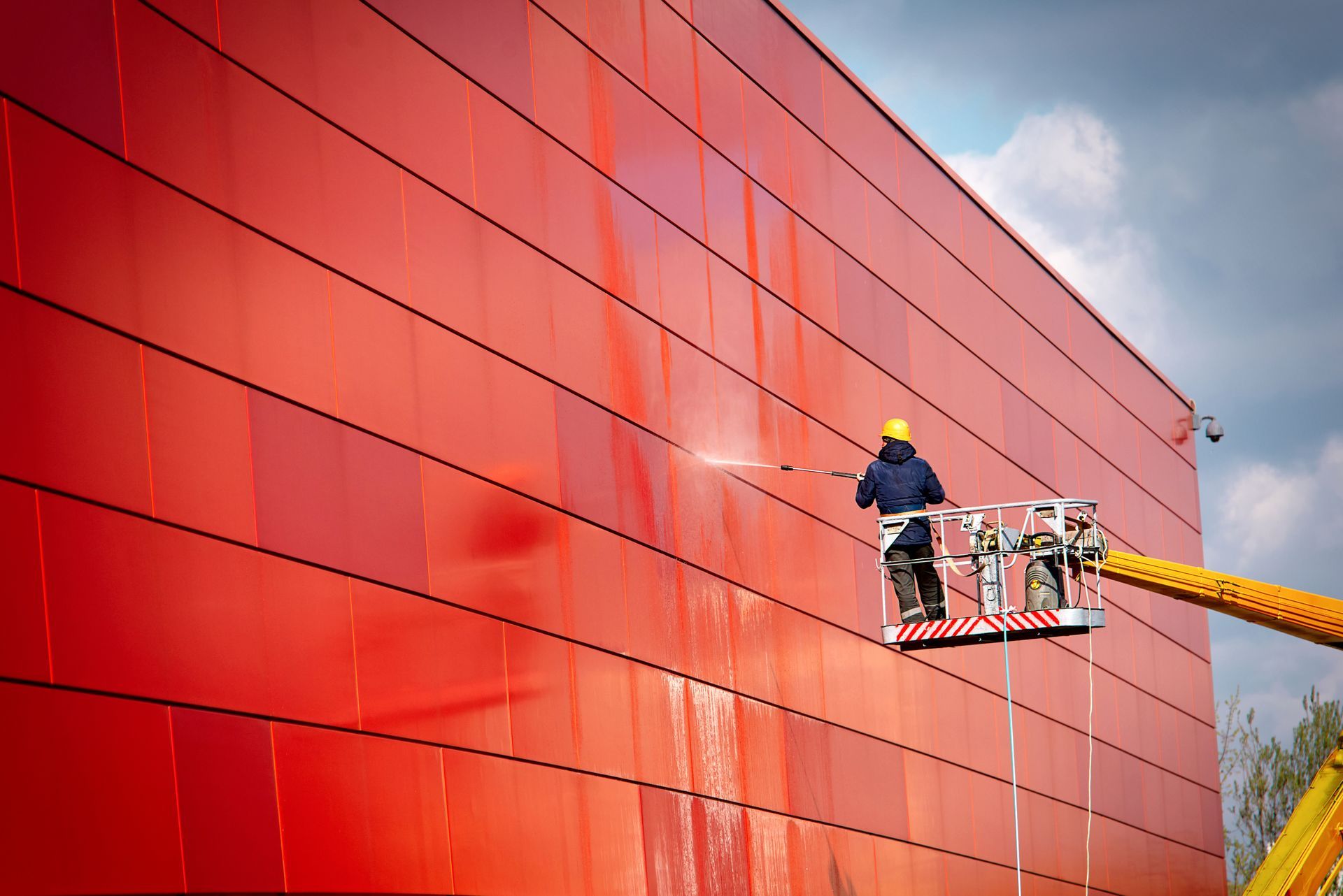 Workers on a cherry picker inspecting a bright red building facade