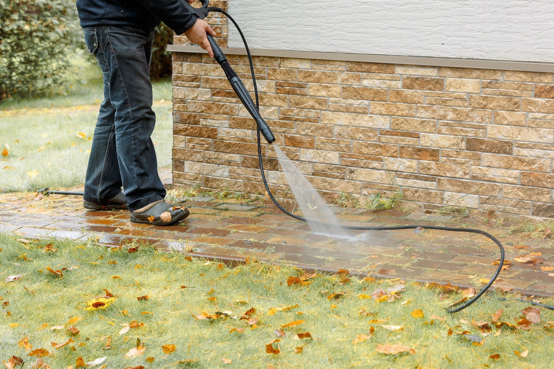 Person pressure-washing a stone wall and wet grass outdoors