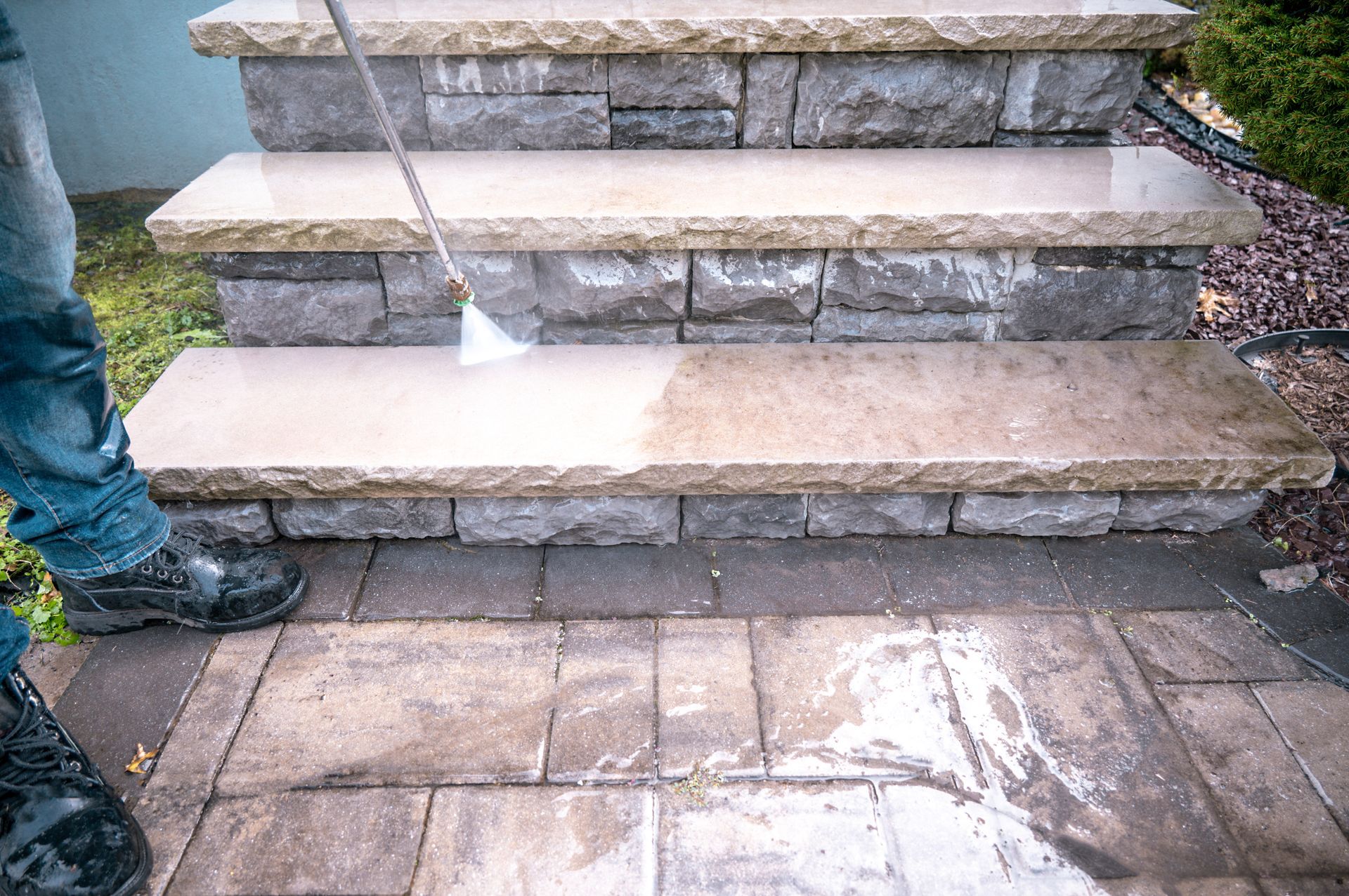 Stone steps and patio being washed with a hose, with water pooling on the wet pavement.