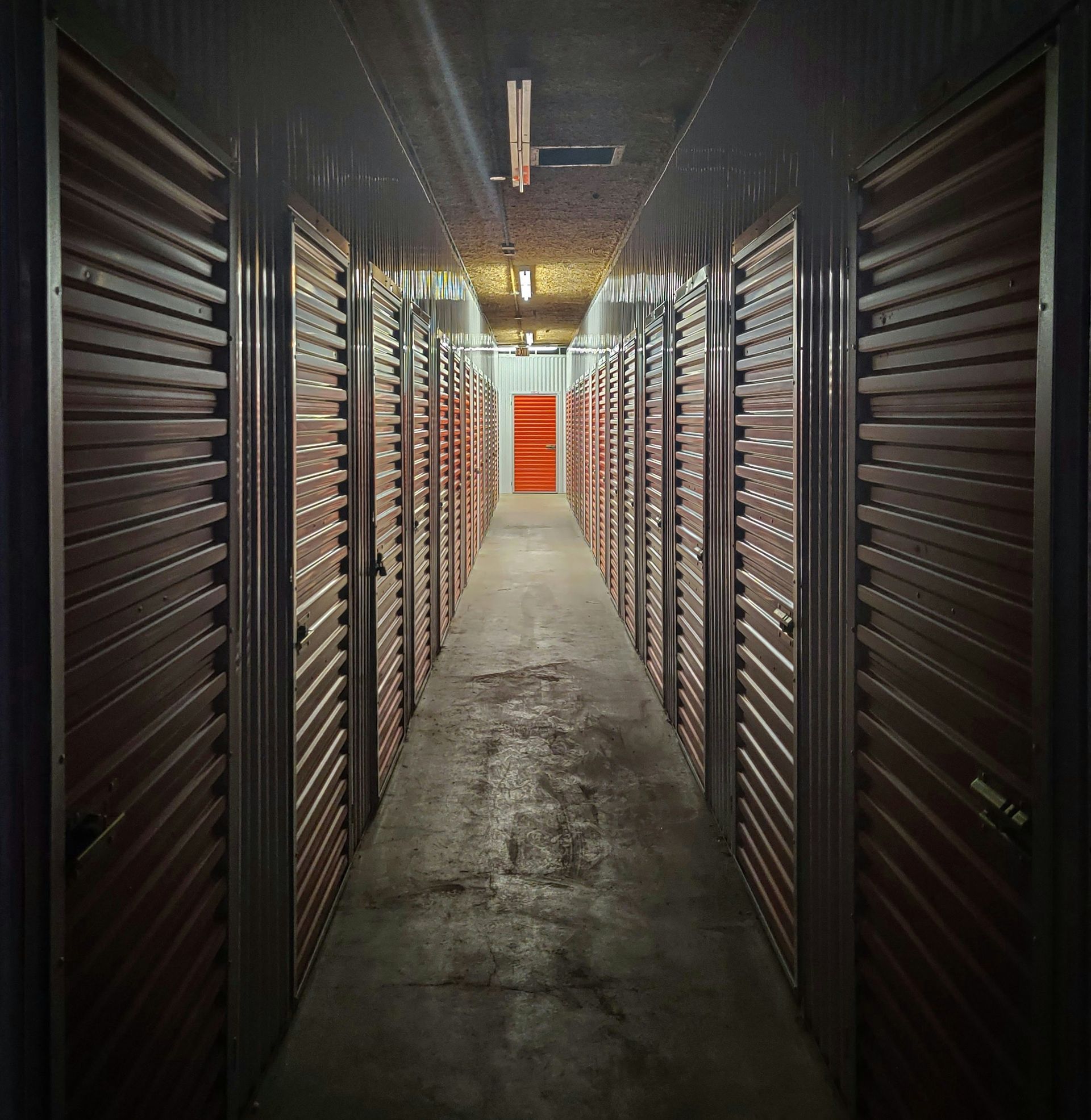 A long hallway with a red door at the end of the storage unit.