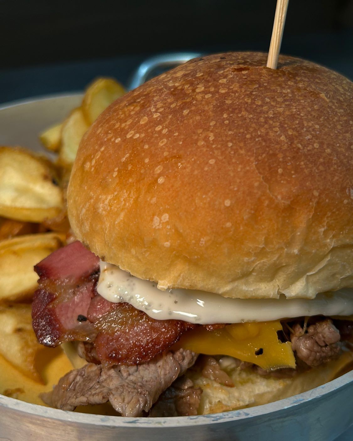 Hamburger con pancetta, uova, formaggio e patatine fritte in una ciotola bianca, tenuti insieme da uno stuzzicadenti.