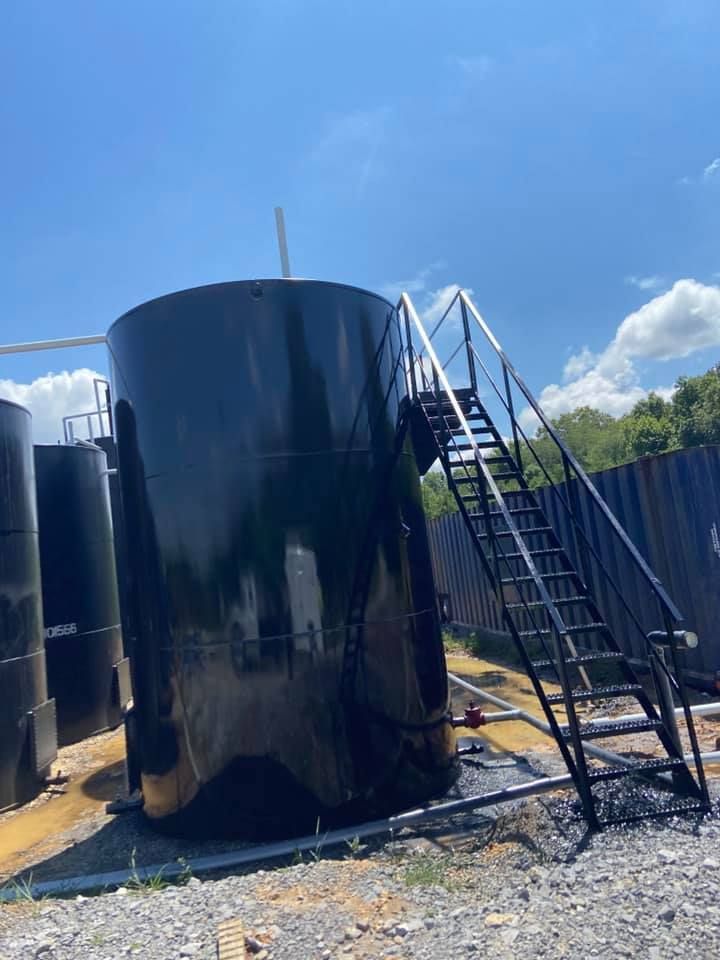 Black industrial storage tank with attached black metal stairs outdoors on a sunny day.