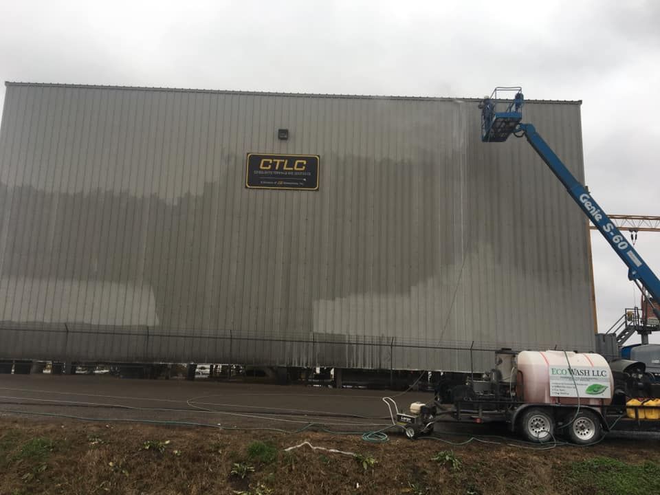 A building being pressure washed by a worker in a lift. A trailer with cleaning equipment is nearby.