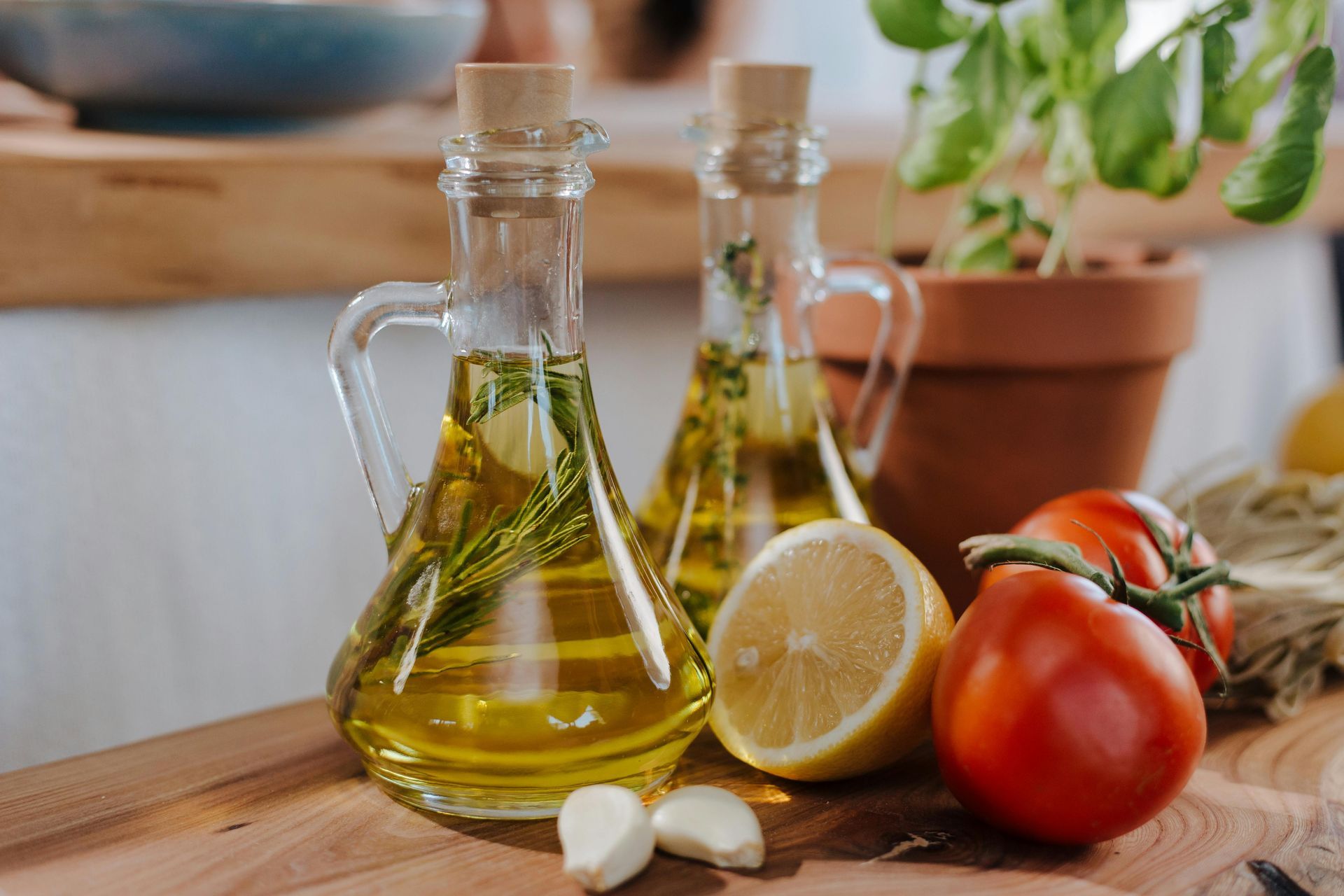 Two glass bottles of oil with herbs, lemon, tomatoes, and garlic on a wooden surface.