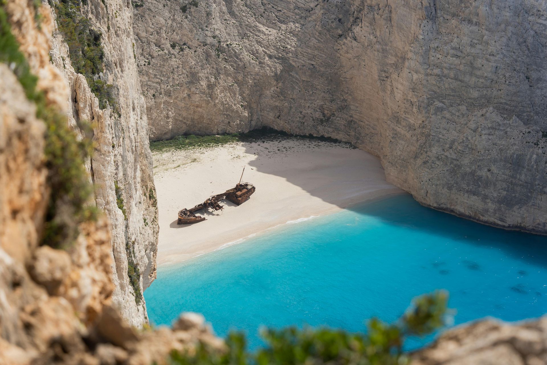 A shipwreck on a white sand beach surrounded by turquoise water and cliffs.