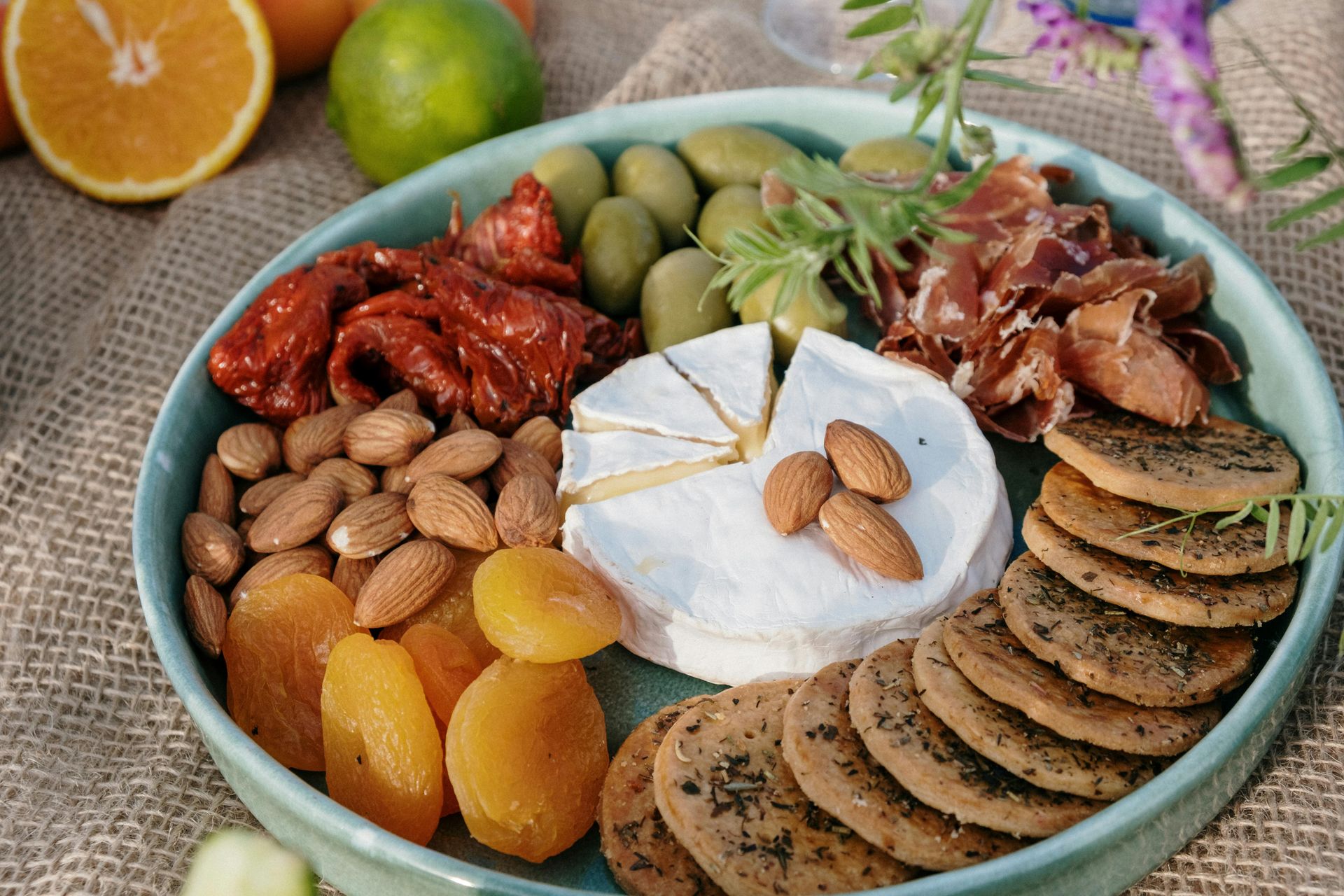 A charcuterie board with cheese, olives, nuts, dried apricots, sun-dried tomatoes, crackers, and prosciutto.