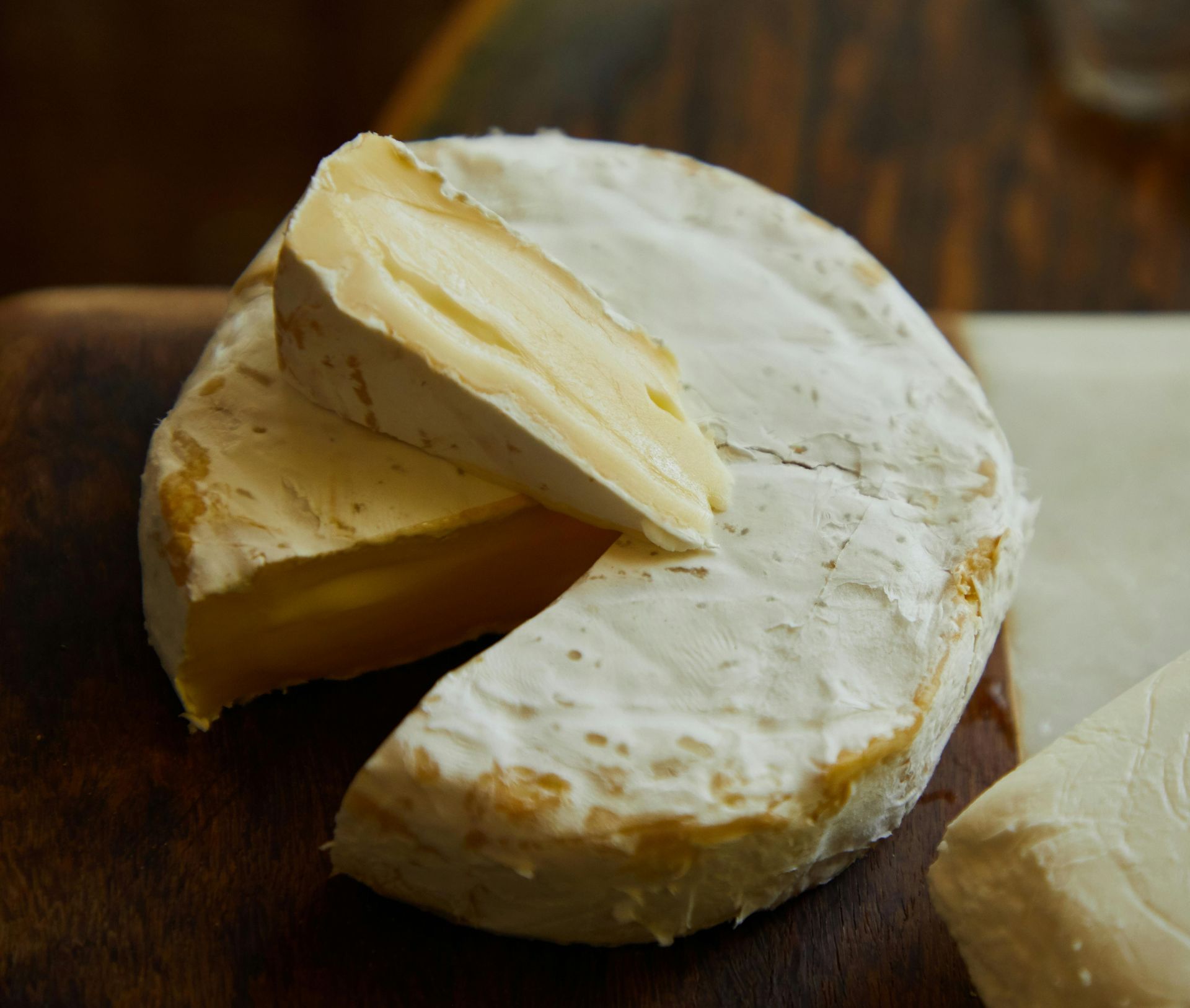 Round of soft cheese with a slice cut out, on a wooden board.