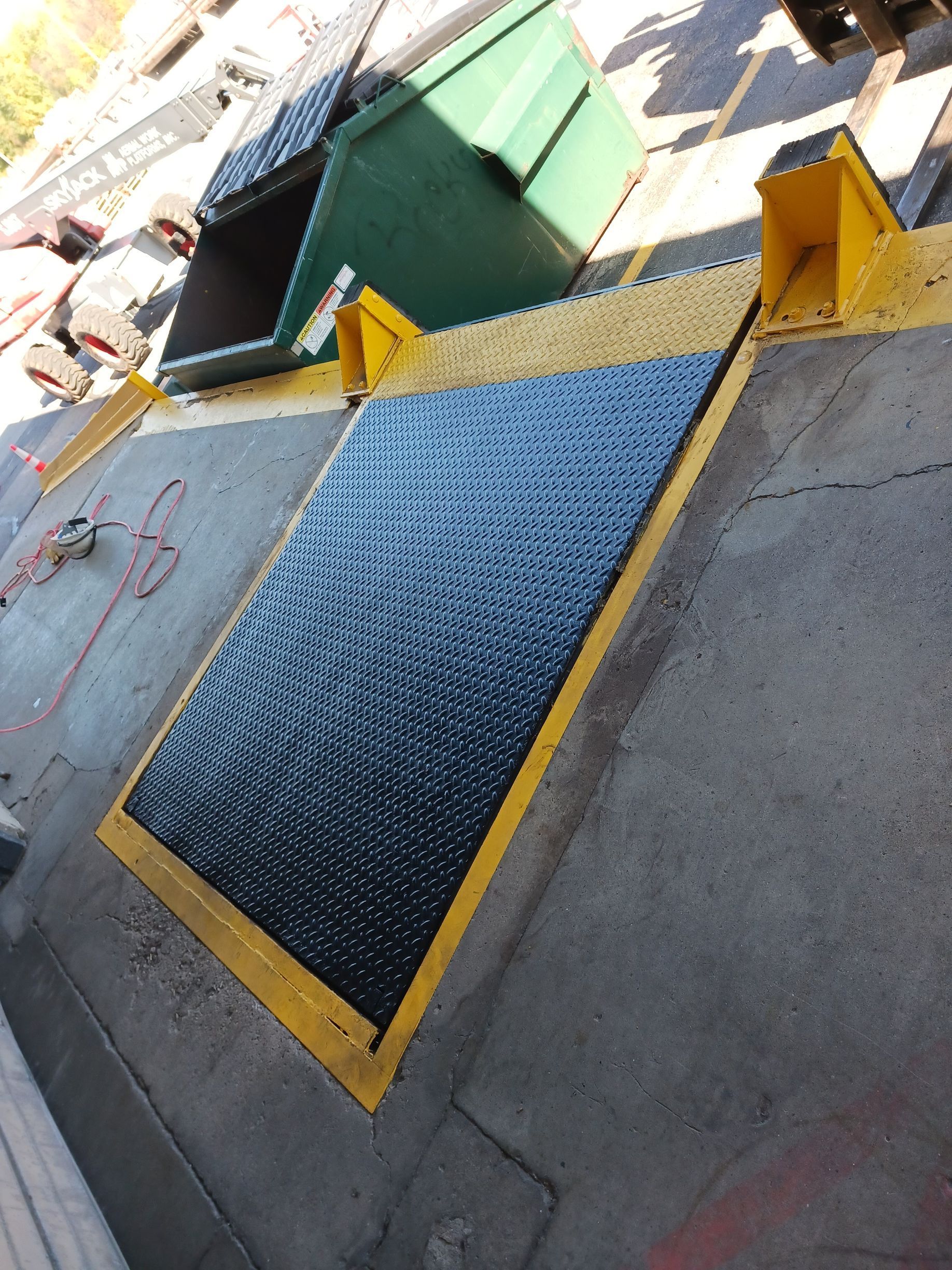 A green dumpster sits next to a black and yellow ramp