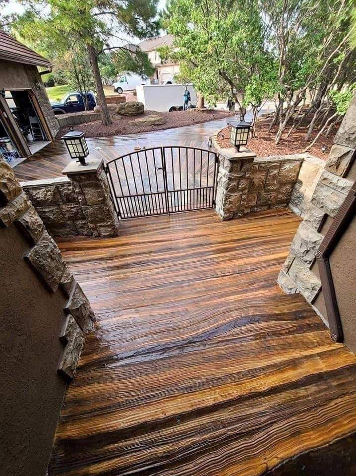A wooden deck with stairs leading up to a stone wall and a gate.