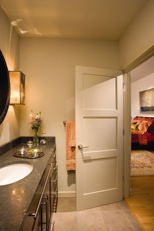 Bathroom with a vanity, sink, open door to a bedroom, and wall sconce.