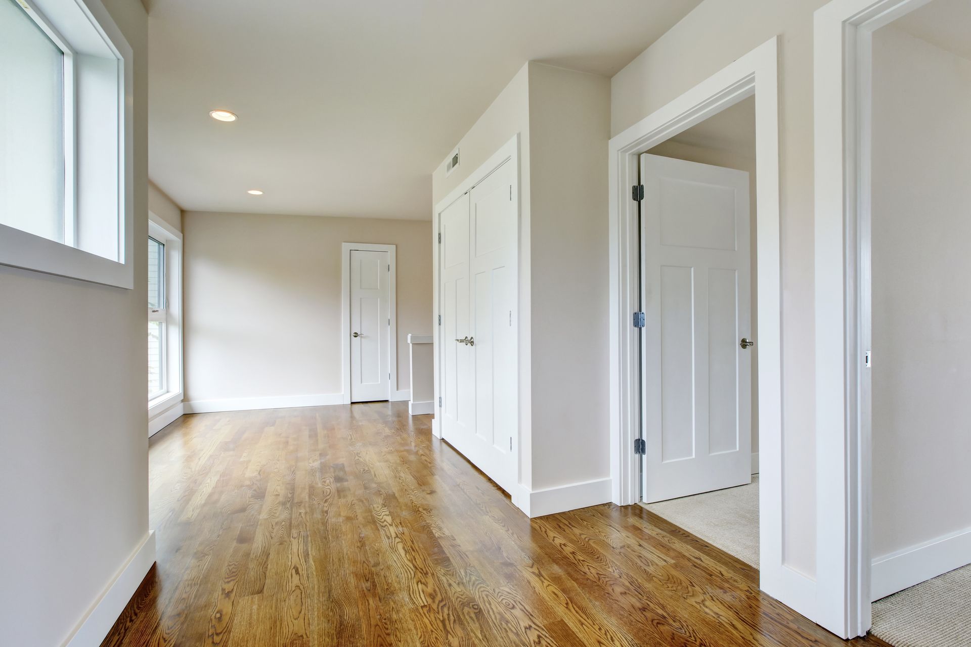 Empty hallway with hardwood floors, white doors, and natural light.