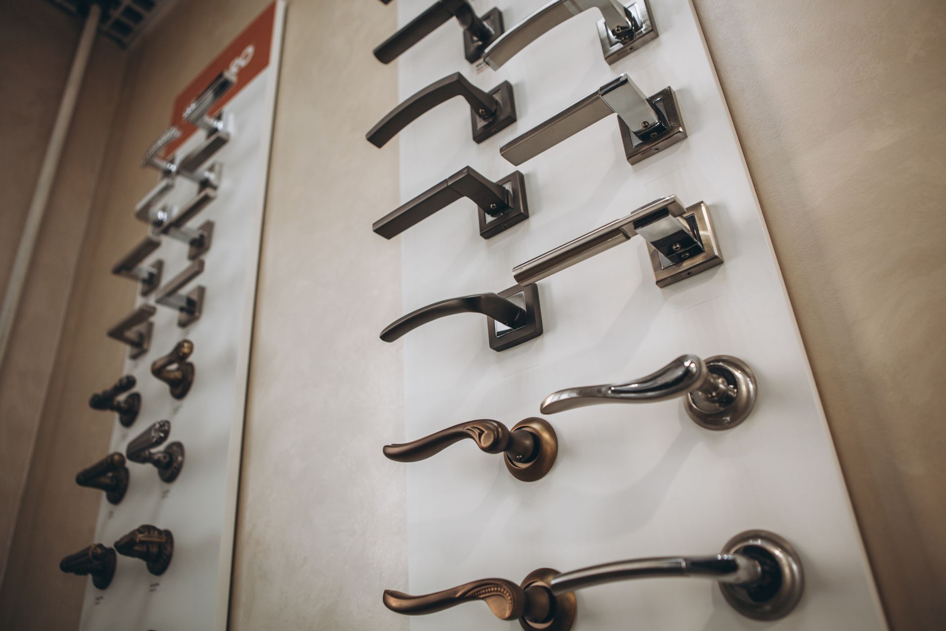 Display of various door handles in a store, mounted on white boards, showcasing different styles and finishes. Display of various door handles in a store, mounted on white boards, showcasing different styles and finishes.