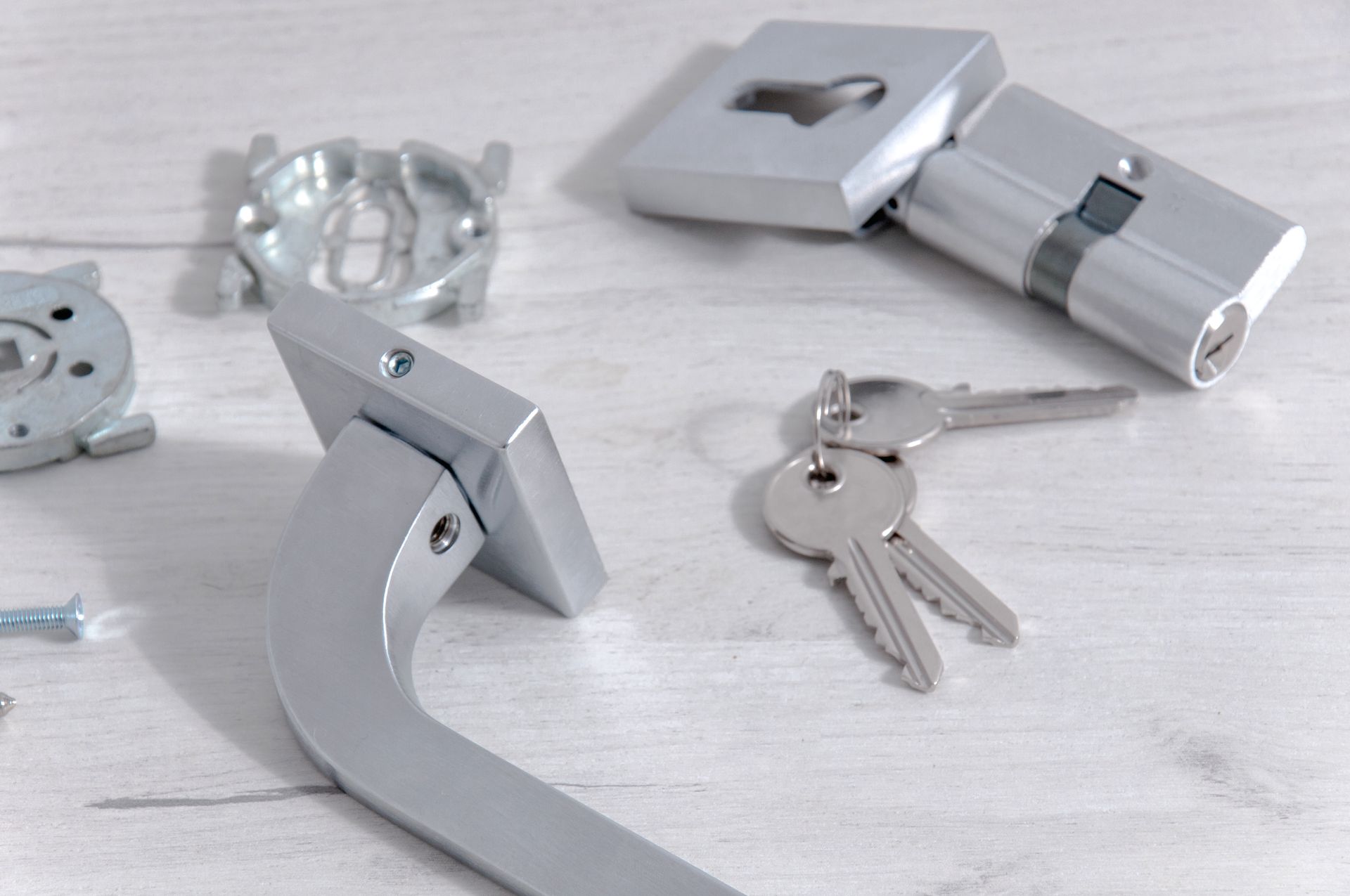 Silver door handle and lock components with keys on a white wooden surface. Silver door handle and lock components with keys on a white wooden surface.