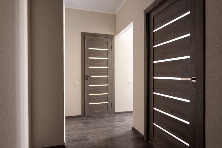 Hallway with three closed wooden doors, gray walls, and dark flooring.