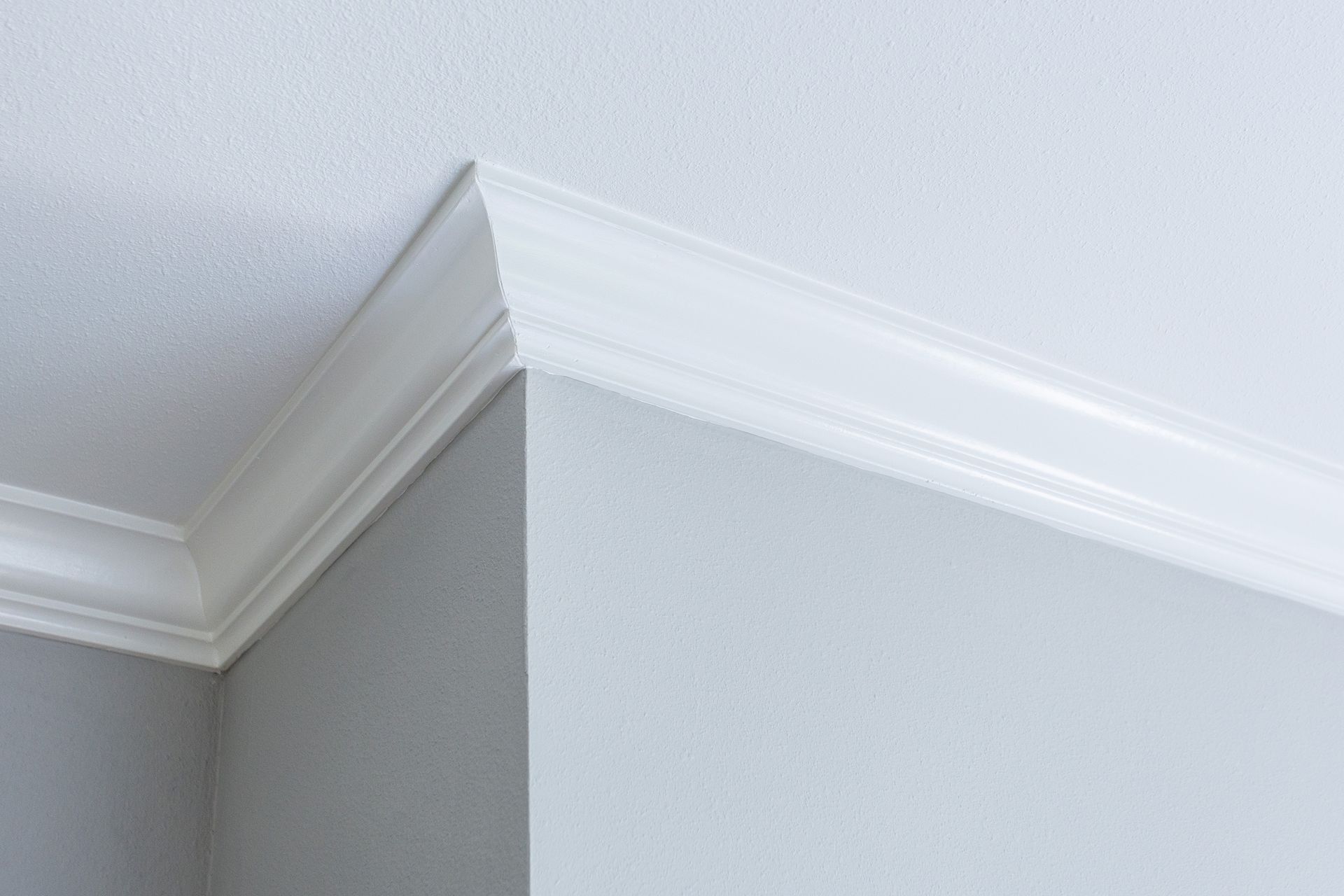 White crown molding at the corner of a ceiling and gray wall.