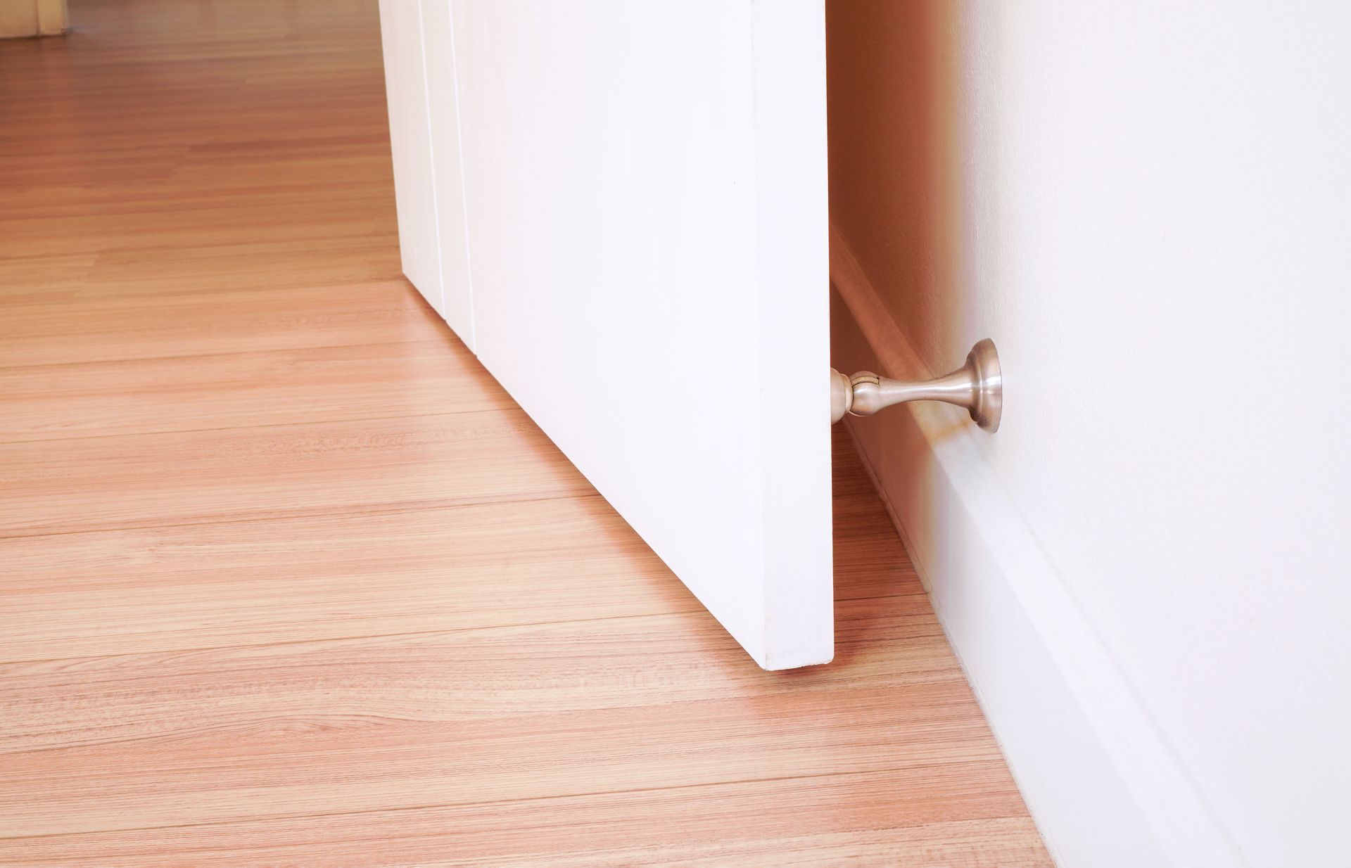White door slightly open, held by a metal doorstop on a white wall, hardwood floor. White door slightly open, held by a metal doorstop on a white wall, hardwood floor.