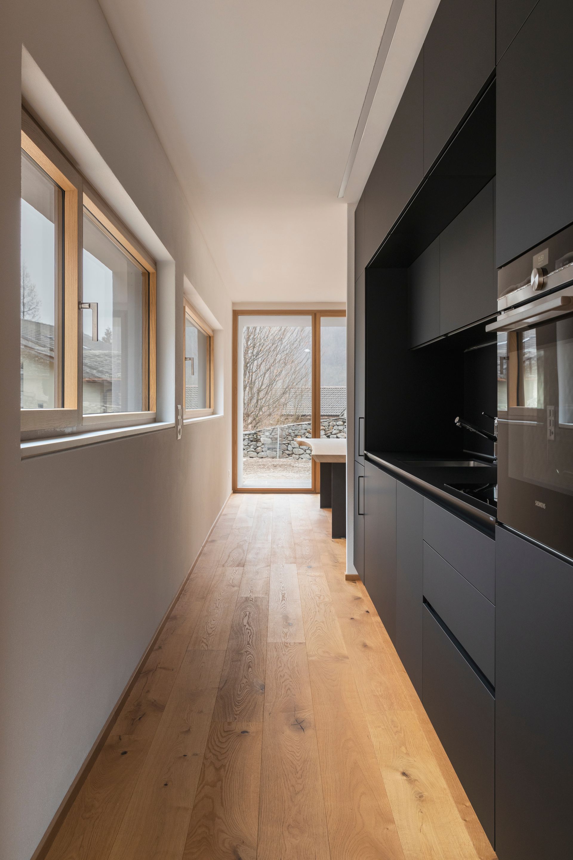 Narrow kitchen with dark cabinets, wooden floor, and windows; a door leads outside. Narrow kitchen with dark cabinets, wooden floor, and windows; a door leads outside.